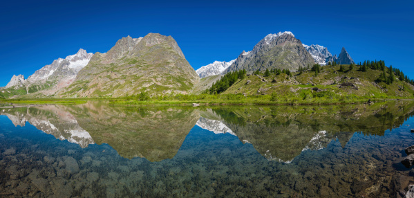 The dramatic rocky pinnacles and snow capped summits of the Mont Blanc massif reflecting in the clear waters of Lac de Combal high in the idyllic summer wilderness of Val Veni on the Tour du Mont Blanc, Aosta Valley, Italy. ProPhoto RGB profile for maximum color fidelity and gamut.