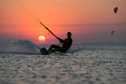 professional kiter makes the difficult trick on a beautiful background of spray and colourful sunset of Black sea