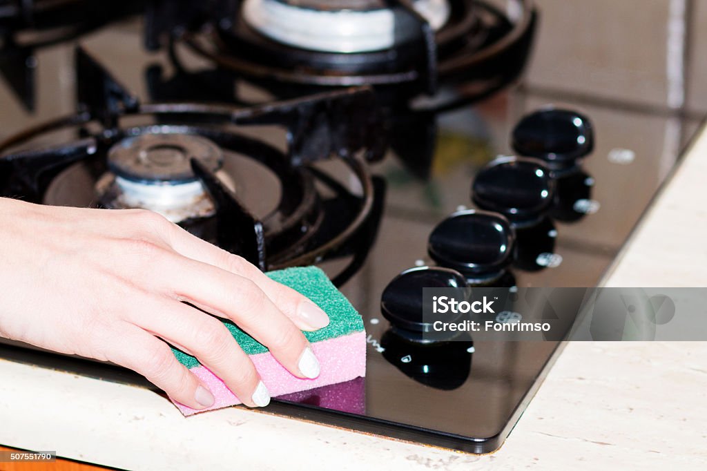 Woman cleaning stove in kitchen Woman rubbing the stove, a woman cleans the stove by pink sponge. woman hand close-up. Woman cleaning stove in kitchen. Camping Stove Stock Photo