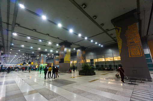 Delhi, India - February 21, 2015: In the middle of the night, outside Indira Gandhi International Airport, a cleaning man is mopping the floor and some people are walking in the background.