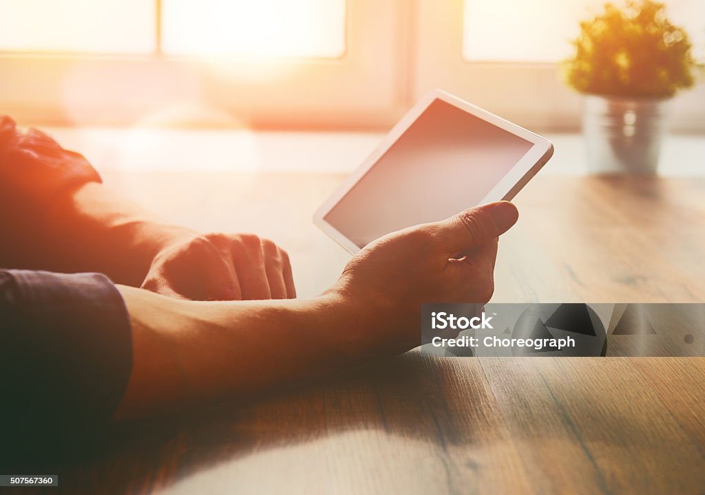 person looking to the digital tablet Thoughtful male person looking to the digital tablet screen while sitting at the table. Digital Tablet Stock Photo