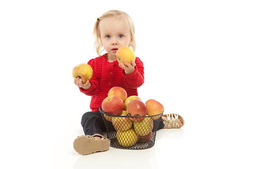 Cute little girl wearing red shirt eating apple on white background.