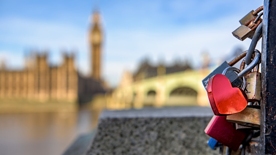 A heart shaped lock connected to other locks near Westminster bridge, Big Ben defocused in the background.