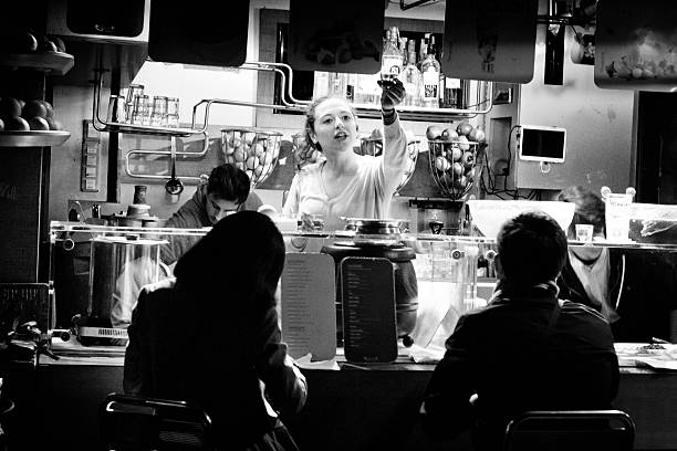 Venice, Italy - April 11, 2015: A waitress picked ot against a cluttered open air bar handing over shot glasses to some tourists out of sight.  