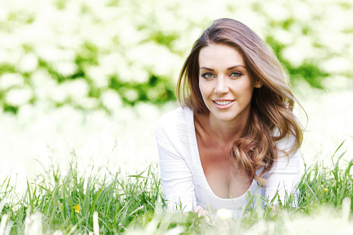 Smiling young woman lying on grass and using smartphone