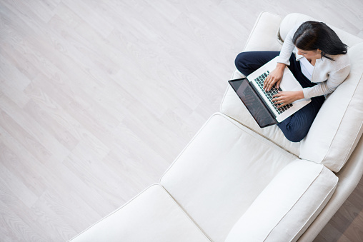 Young woman working at home on her laptop computer lying on the couch