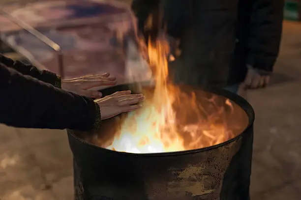 Photo of Homeless man warming his hands by a fire