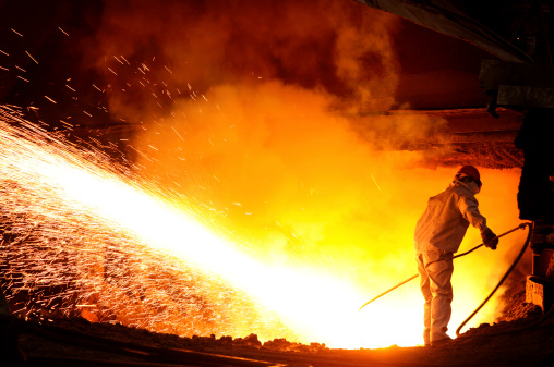 An operation worker in orange coverall is holding white safety helmet or hardhat with factory place as background. Safe working practice in the industrial scene photo, close-up and selective focus.