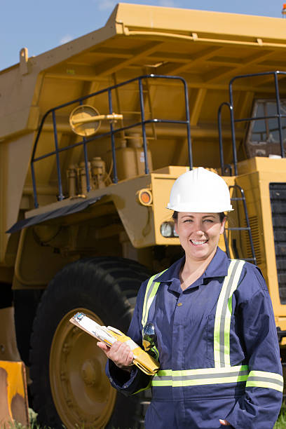 Female oil or construction worker in front of hauling truck A royalty free image of an attractive female blue or white collar worker from either the oil or construction industry smiling, friendly and happy while standing in front of a massive hauling truck.  This image could be used in the transportation industry.  She is wearing a hardhat and has safety equipment and safety glasses displayed. oilsands stock pictures, royalty-free photos & images