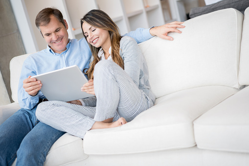 Happy couple at home sitting on the couch using a tablet computer and smiling