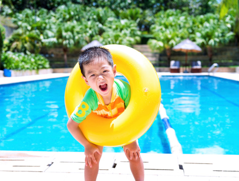 little boy standing in front of pool with a yellow swimming tube.
