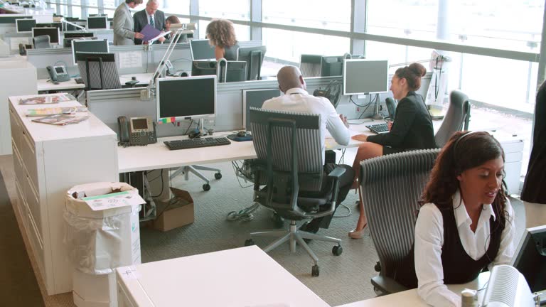 Colleagues talking at a desk in a busy open plan office