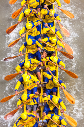 Bangkok, Thailand - December 12, 2010: The Thai male participants in their jerseys during a traditional dragon boat races on the Chao Phraya River in Bangkok. With her piercing paddling equipped, they try to win the competition in their boats. Depending on the type and size of the boat, sit together in pairs by up to 50 oarsmen with their piercing paddling. This photo was taken from the bridge Rama VIII. The dragon boat is a particularly long, open canoe, which originated in
