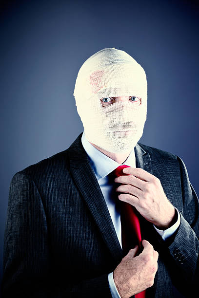 istock Businessman with bandaged head, face obscured, adjusts his tie 507619467