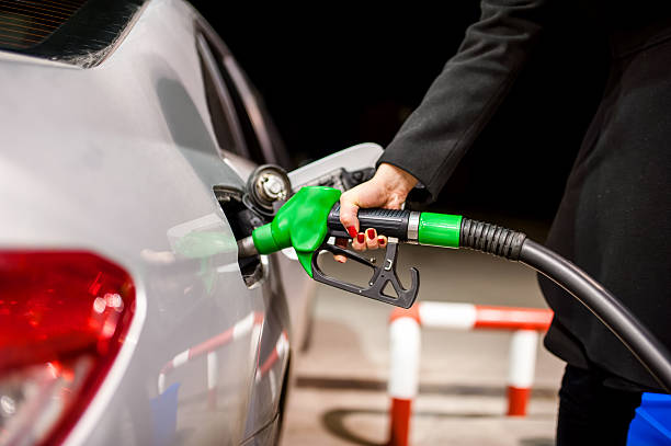 молодая женщина, бьющая газа в автомобиль на бензин станции - gas fuel pump labeling fuel and power generation стоковые фото и изображения
