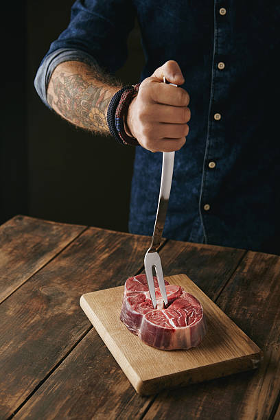 istock butcher hand holds meat fork in raw steak 507632352
