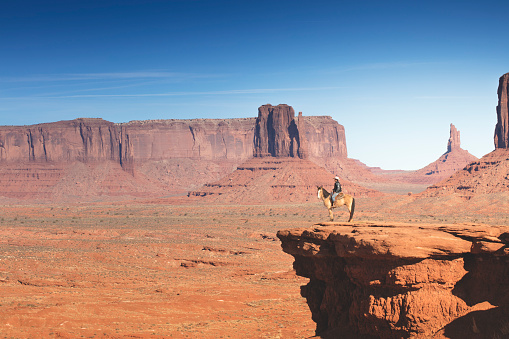 A photograph of a Navajo Native American riding a horse in Monument Valley, Arizona. Monument Valley can be seen in the background while the horse and its owner have stopped on the edge of a cliff. Photographed with the Canon EOS 5DSR at 50mp.