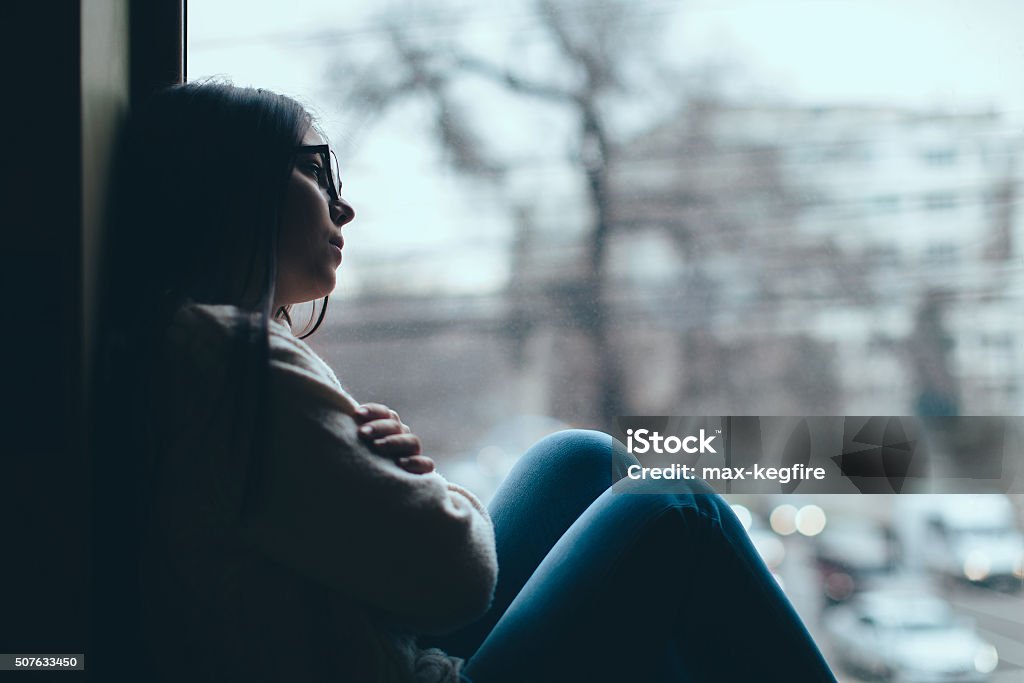 Teenage girl looking out the window Silhouette of sad teenage girl looking out the window on a cold autumn day Sadness Stock Photo