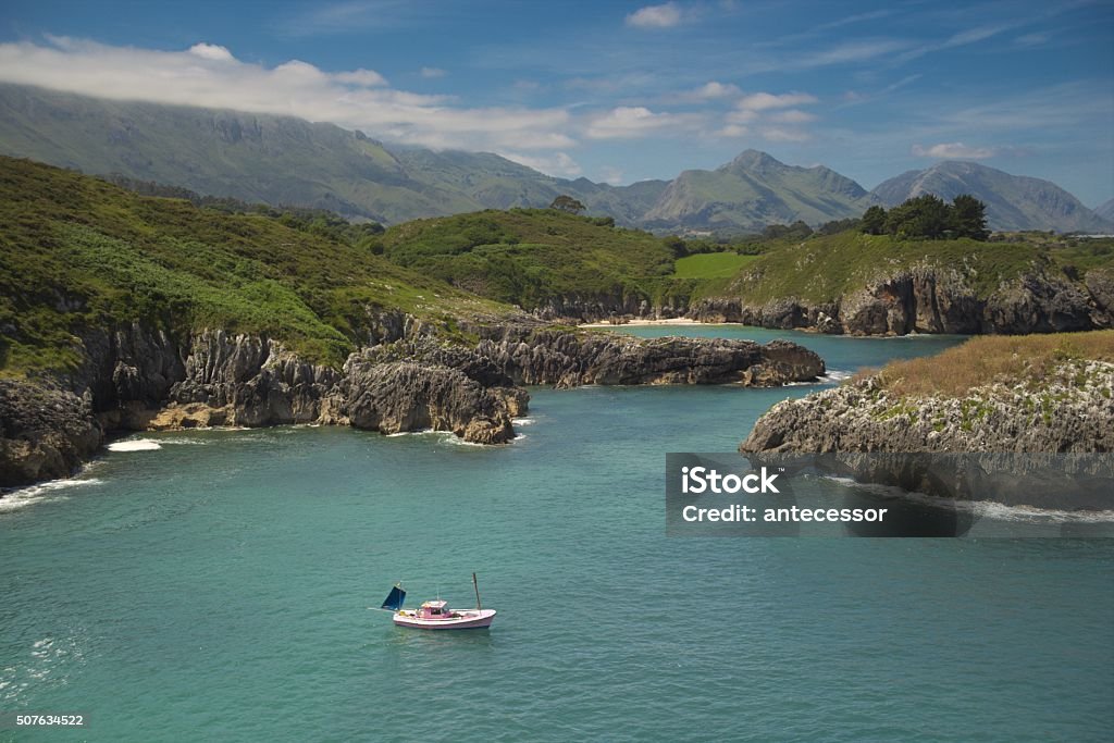 The boat that is close to the shore and mountain A peaceful and sunny day in Asturias (Spain). The tranquility than can be breathed is astonishing. The sea is quite calm, and the boat doesn't rock. Otherwise, the mountains, just a few meters from the shore, are foggy at their peaks. Asturias Stock Photo