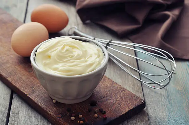 Homemade mayonnaise in bowl with eggs and spice on wooden background