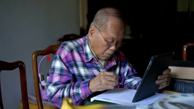 Old man writing information out of digital tablet