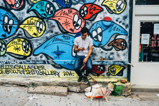 New York City, United States - August 17, 2014: Young man looking at the phone while walking the dog in Williamsburg, Brooklyn.