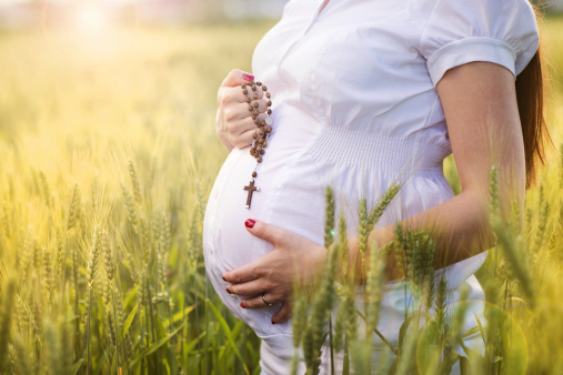 Outdoor portrait of unrecognizable young pregnant woman praying in the field