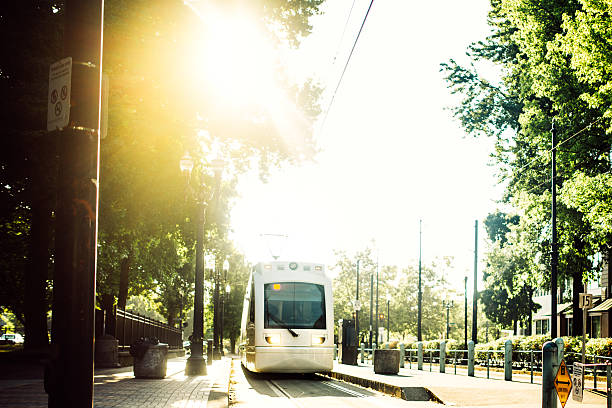 The MAX Line: Rail train public transportation in Portland Oregon traveling on the Clackamas route pulling out from the park and ride.  Bright vibrant morning light with green and blue colors.  Horizontal with copy space.