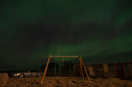 The aurora borealis light up the skies over an abandoned swing set.