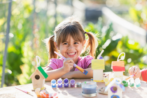 Little girl (3 years, Hispanic) painting little wooden bird feeder.