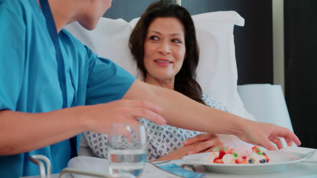 Female Patient In Hospital Bed Being Served Meal By Orderly