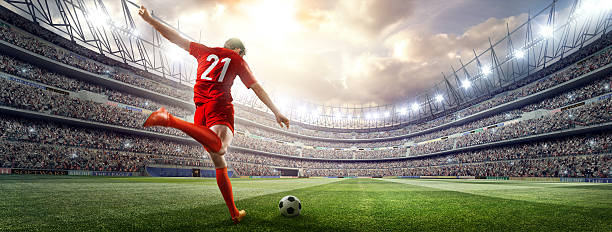 Soccer player kicking ball in stadium A male soccer player makes a dramatic play by kicking a ball with his feet. The stadium is blurred behind him. It's sunny weather. kicking photos stock pictures, royalty-free photos & images