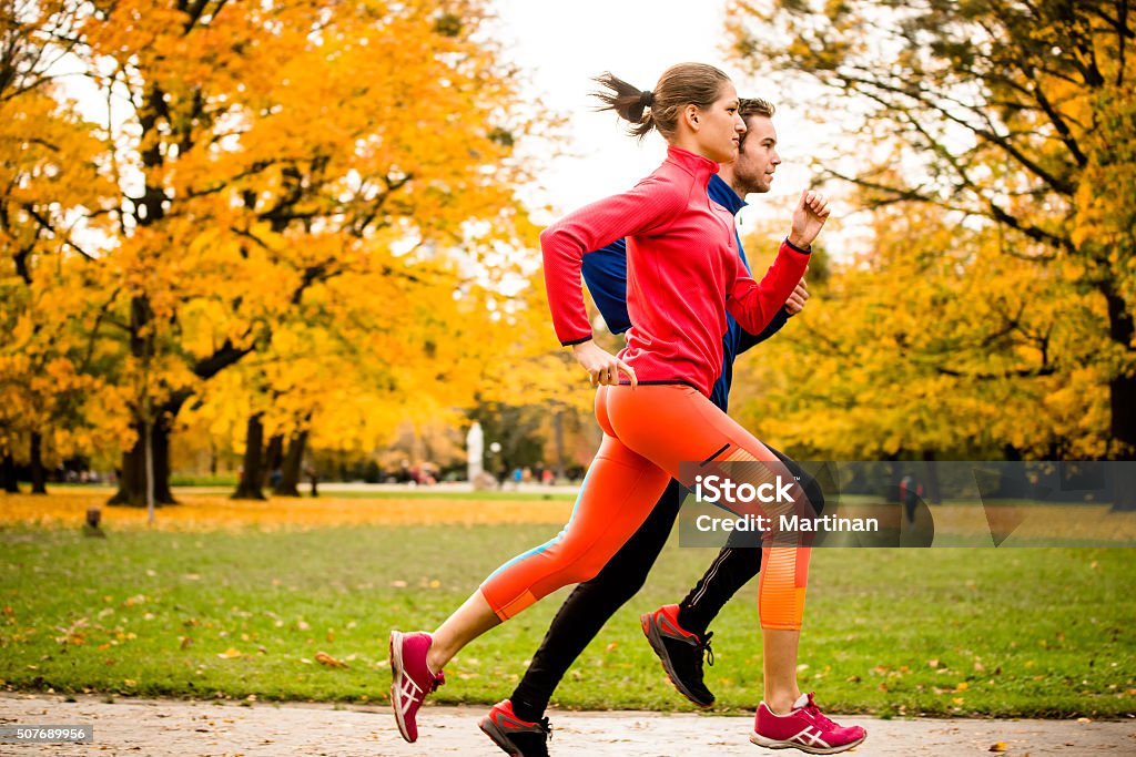 Couple jogging in autumn nature Young couple jogging together in park - rear view Running Stock Photo