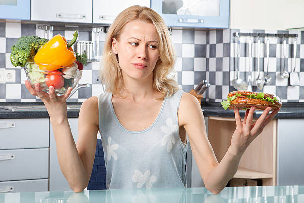 istock Woman choosing between vegetables and sandwich 507706836