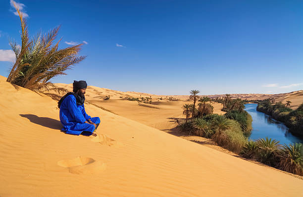 Tuareg on dune , Um el Ma , Mandara lake , Sahara, Libya Awbari, Libya - November 06, 2007: Tuareg sits on a sand dune in the Libyan desert, view to the Mandara Lakes (Um el Ma), Sahara, Libya. um el ma oasis stock pictures, royalty-free photos & images