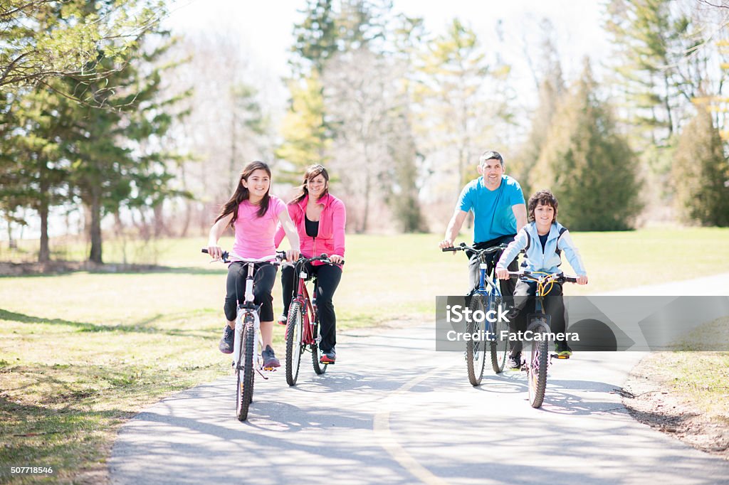 Biking Happily Through the Park A family of four is biking together through the park on a beautiful sunny day. Family Stock Photo