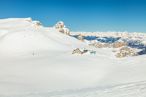 Boè hut sunk in snow on the Dolomites.  Wilderness area near Pordoi.  Ski tracks and a blue clear sky in background