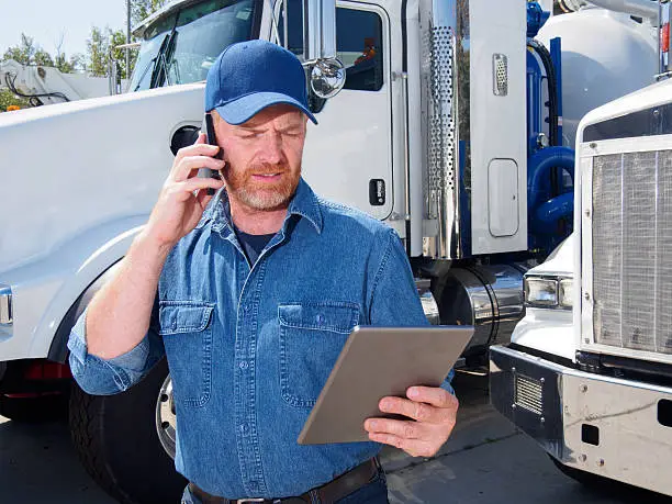 A royalty free image from the trucking industry of a truck driver using a smartphone and tablet computer.