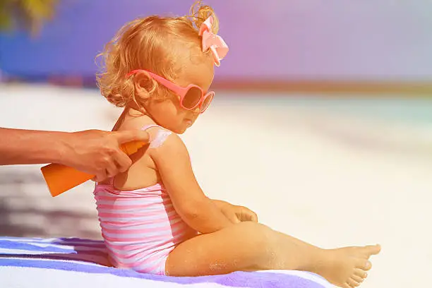 Photo of mother applying sunblock cream on daughter shoulder