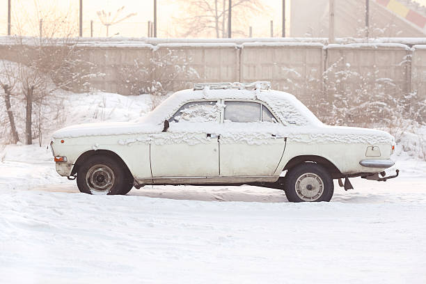 Abandoned car covered with snow in winter at sunset, warm stock photo