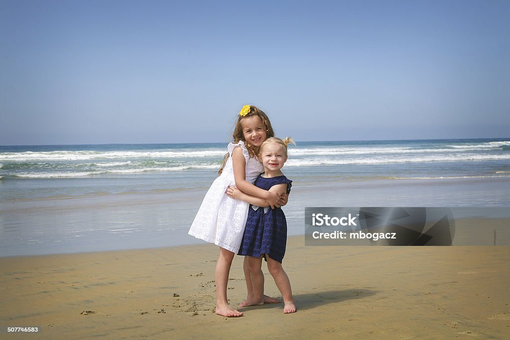 Sisterly Love, Beach Scene Image of 2 little girls.  One is 5 and other almost 2 posing on the beach.  Hugging each other showing their affection. 18-23 Months Stock Photo