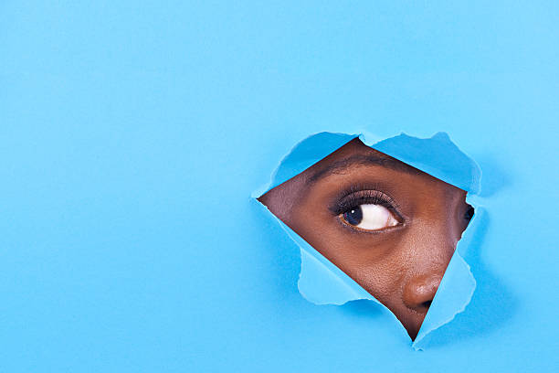 Is there something there? A view of a woman's eye looking through a hole in some colorful paper finding stock pictures, royalty-free photos & images