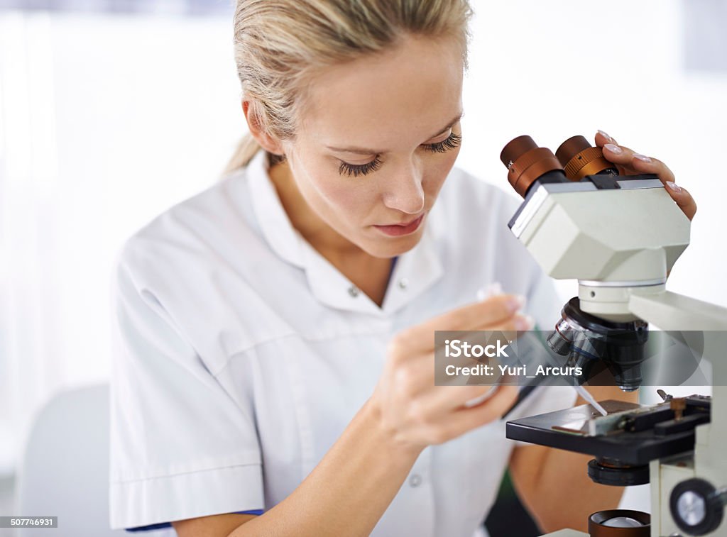 Serious about finding a cure Shot of a beautiful woman in a laboratory working with a microscope Adult Stock Photo