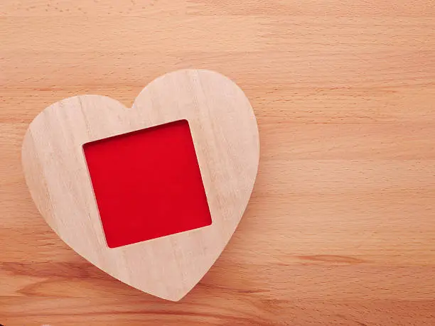 Wooden picture frame with love heart on wooden background.