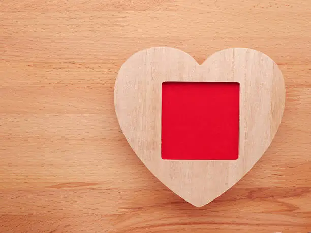 Wooden picture frame with love heart on wooden background.