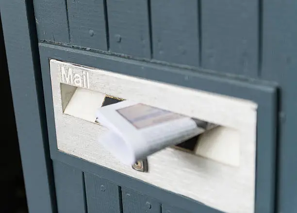 Color image of a periodic, daily newspaper pushed into a mailbox