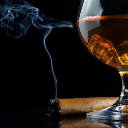 Snifter glass of cognac and cigar on black