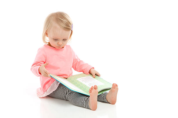 Baby girl reading a book while sitting on a hardwood floor