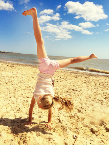 Happy little girl doing a cartwheel on an English beach in the summer