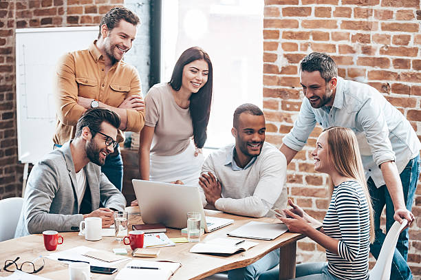 Successful team. Group of cheerful young people discussing something with smile and gesturing while leaning to the table in office stubble male african ethnicity facial hair stock pictures, royalty-free photos & images